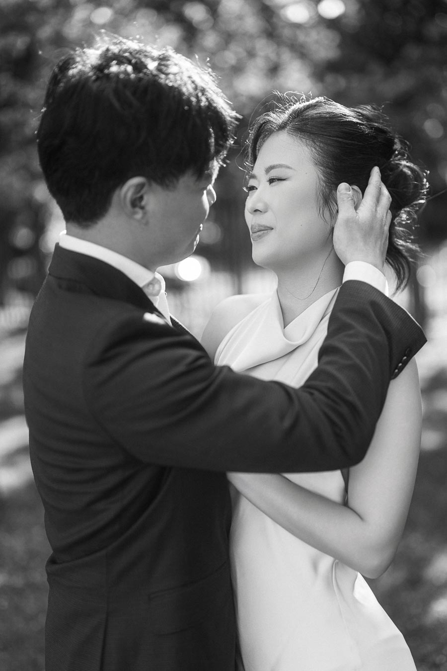 Black and white photo of an engaged Asian couple at Trillium Park, Toronto. The groom-to-be gently touches the bride-to-be's face, both sharing a loving moment outdoors.