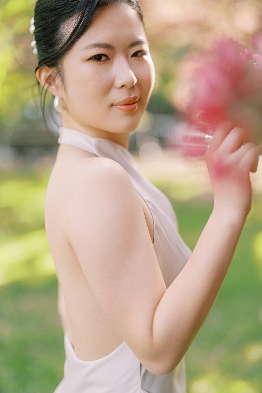 Close-up of an Asian bride-to-be in a white dress, holding pink blossoms at Trillium Park, Toronto, with a soft natural background.
