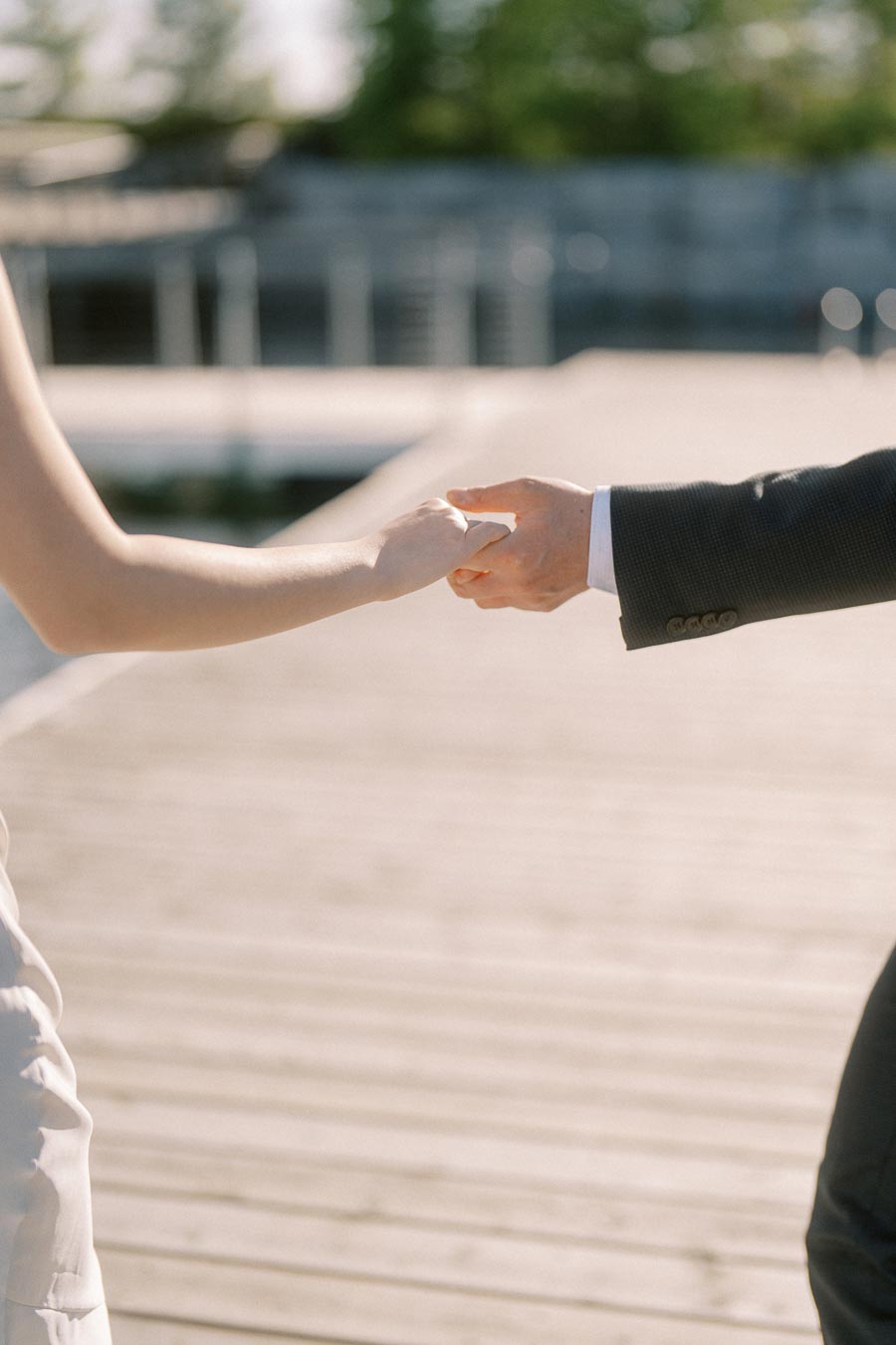 Close-up of an engaged couple holding hands on a wooden boardwalk at Trillium Park, Toronto, with soft sunlight and a romantic, elegant atmosphere.