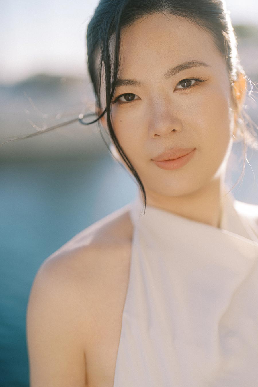 Close-up portrait of an Asian bride-to-be in a white dress, softly smiling with sunlight on her face, photographed at Trillium Park by the Toronto waterfront.