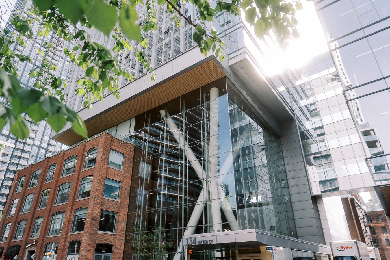 Exterior of The Atrium at Ricarda’s, Toronto, showing glass facade, brick building, and leafy branches in foreground.