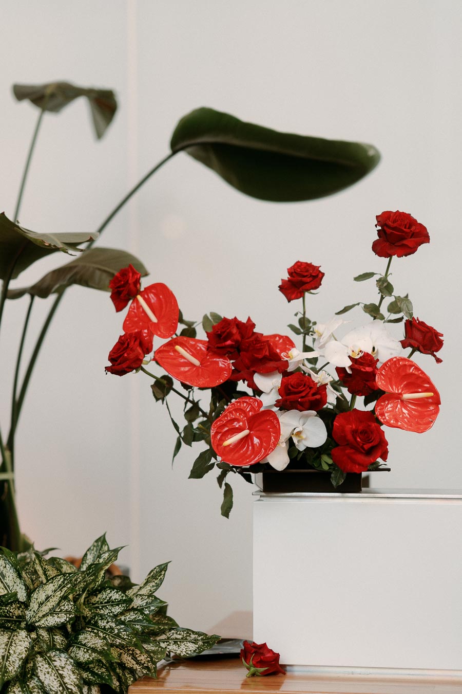 Red roses, red anthuriums, and white orchids arranged in a modern centerpiece with tropical leaves, displayed at Ricarda’s Toronto event venue.