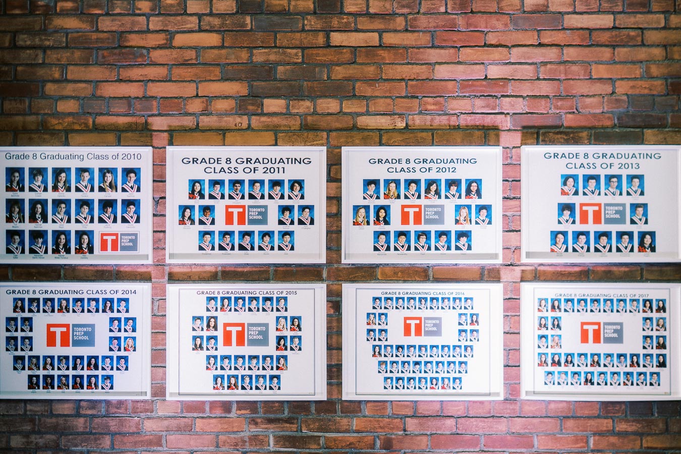 Framed Toronto Prep School Grade 8 graduating class photos from 2010 to 2017 displayed on a brick wall at Ricarda’s in Toronto.