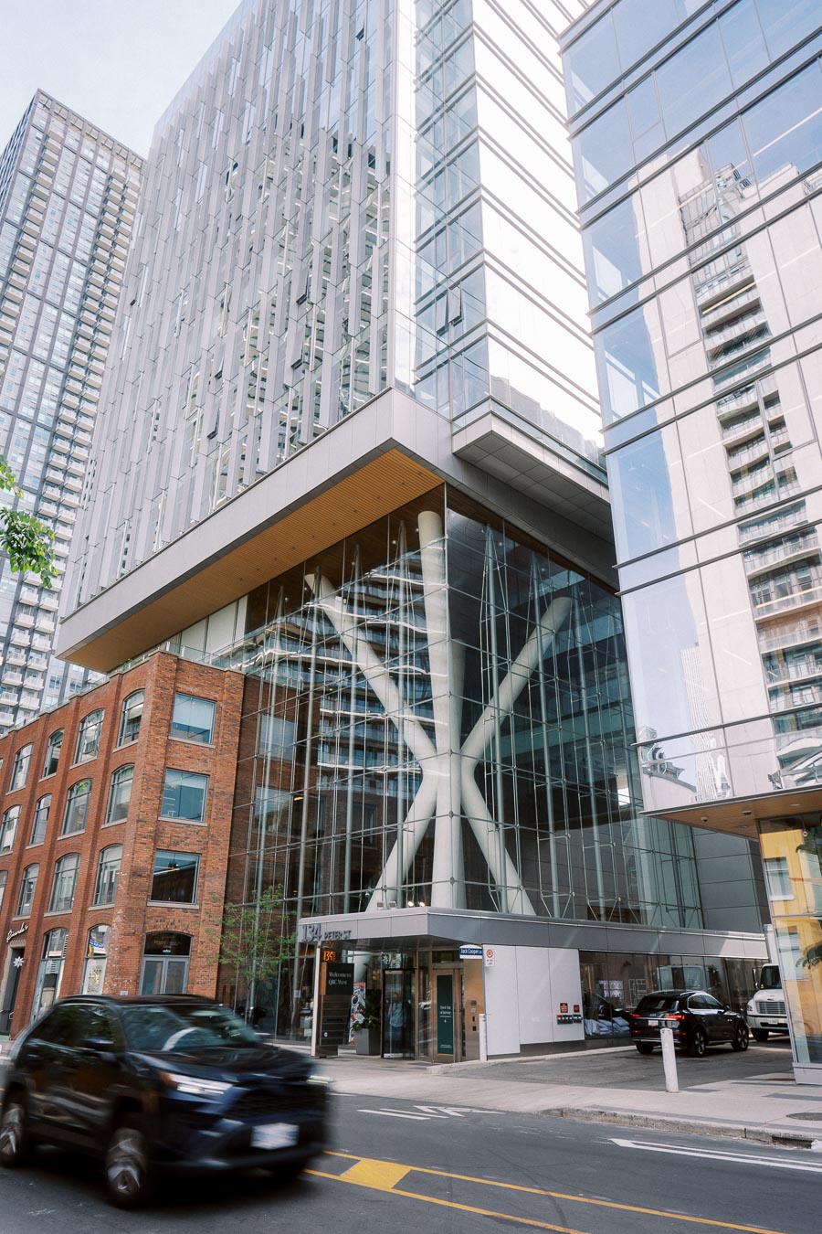 Street-level view of Ricarda’s Restaurant at 134 Peter Street, Toronto, featuring a modern glass atrium, brick facade, and passing cars, photographed during a school event.