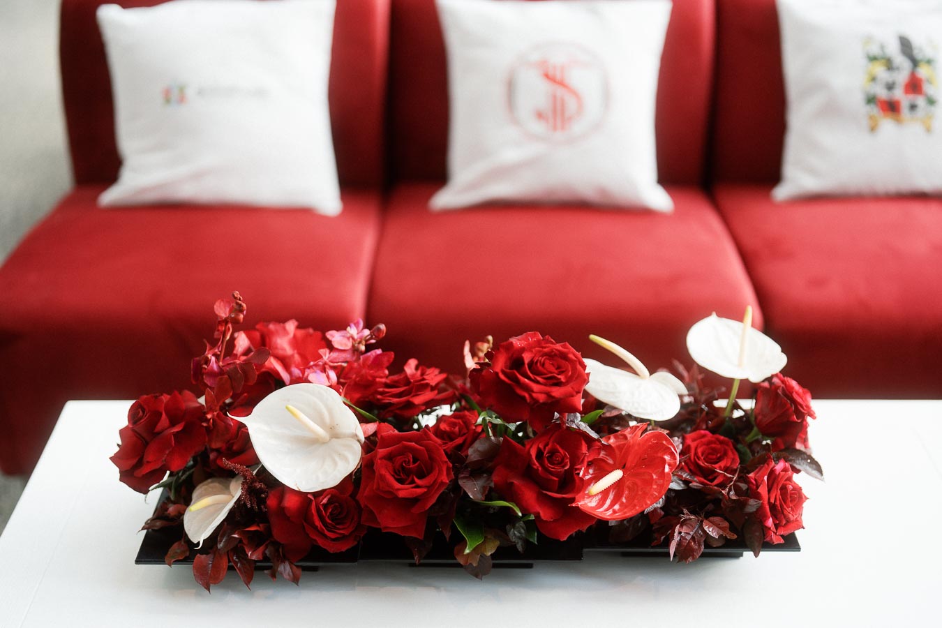 Red and white floral arrangement on a white table with red couches and Toronto Prep School branded pillows in the background at Ricarda’s Toronto event.