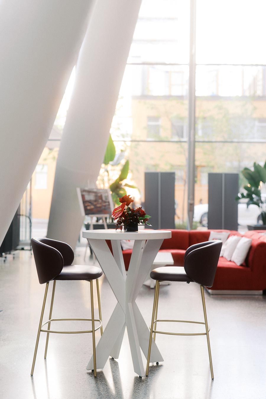 Contemporary white cocktail table with two chairs and a red floral centerpiece in the bright atrium at Ricarda’s, Toronto, photographed during a school launch event.