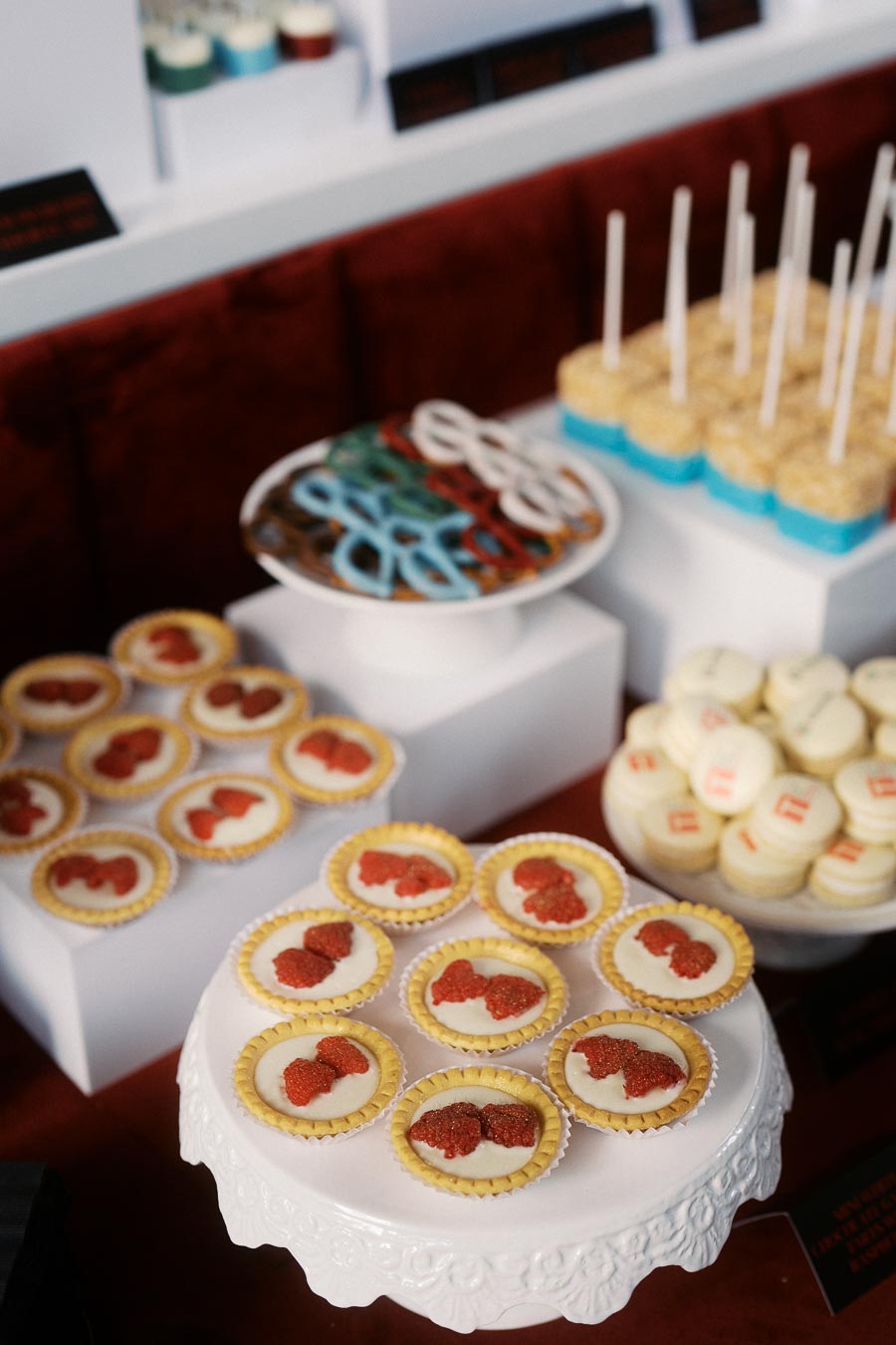 Assorted Toronto Prep School branded desserts, including tarts with red logos and macarons, displayed on white stands at Ricarda’s event venue in Toronto.