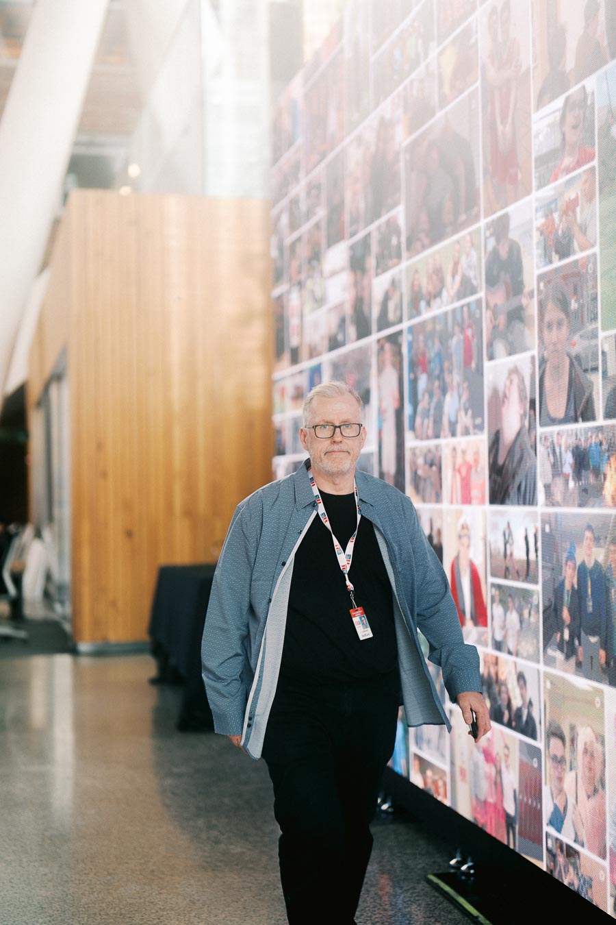 A man with glasses and a lanyard walks beside a wall of community photos at Ricarda’s during the Toronto Prep Forever Launch Party.
