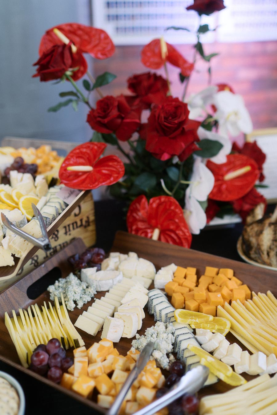 Assorted cheese platter with grapes and lemon slices, set next to a bouquet of red and white flowers at Ricarda’s in Toronto during a school launch event.