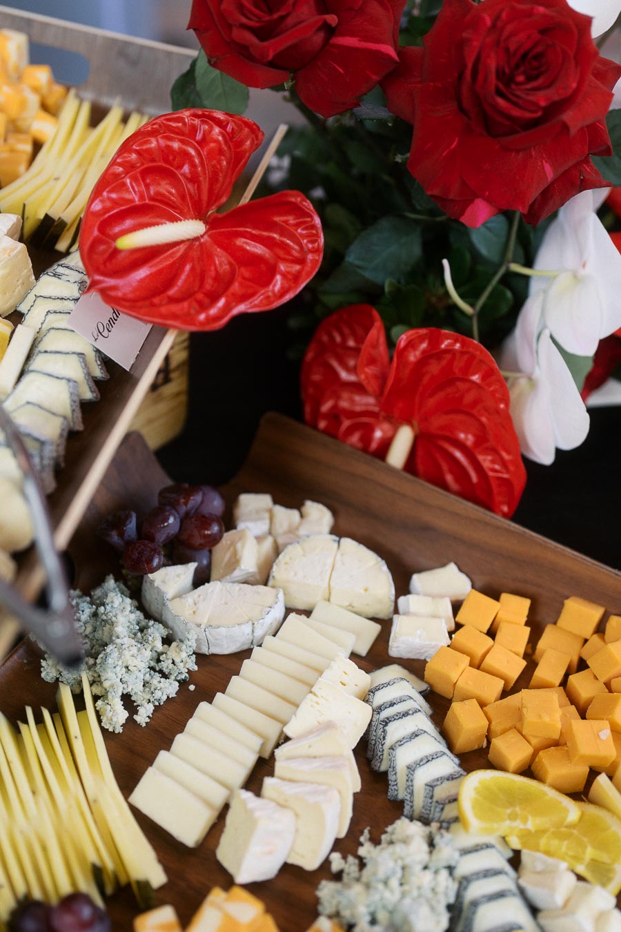 Assorted cheese platter with grapes and lemon slices, set beside red roses and anthurium flowers at Ricarda’s during a Toronto school launch event.