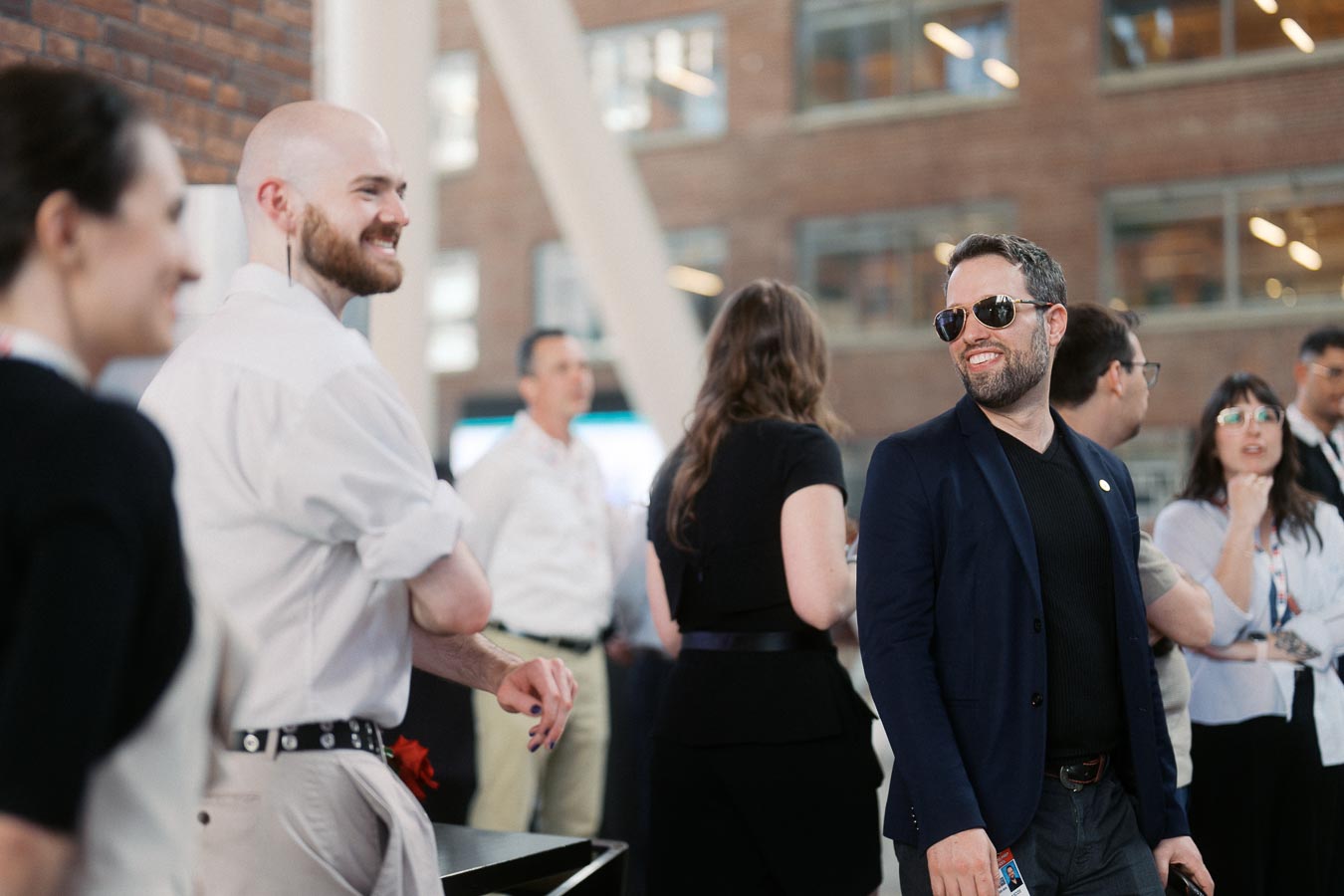 A group of adults, casually dressed, engage in lively conversation at Ricarda’s during the Toronto Prep Forever Launch Party. Brick walls and large windows are visible in the modern venue.