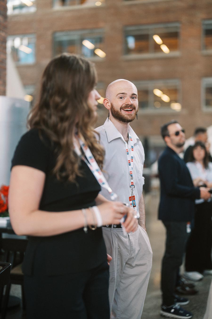 Two guests with Toronto Prep School lanyards converse at the Toronto Prep Forever Launch Party in Ricarda’s Atrium, Toronto, with others mingling in the background.