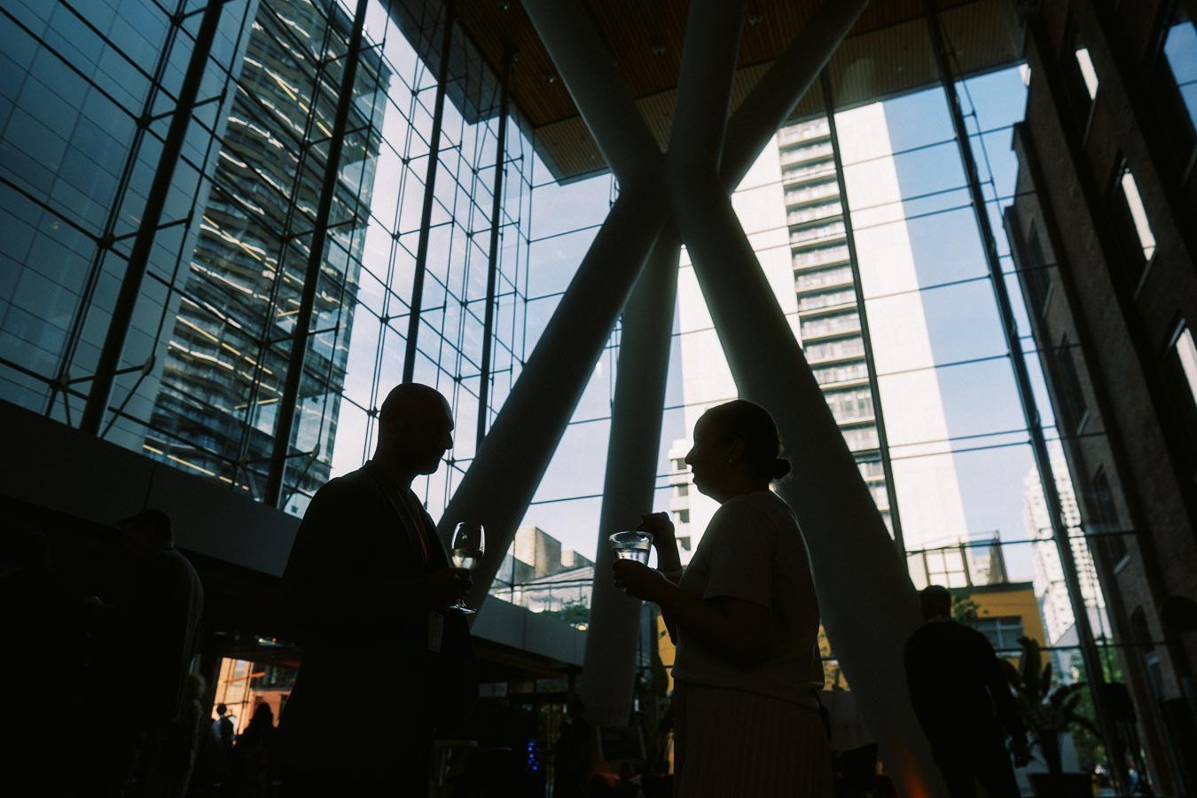 Silhouetted guests with drinks networking inside the glass-walled Atrium at Ricarda’s, Toronto, during the Toronto Prep Forever Launch Party.