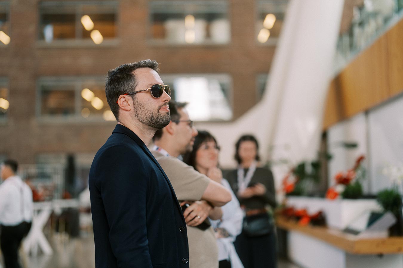 A man in a navy blazer and sunglasses stands with other guests inside The Atrium at Ricarda’s during the Toronto Prep School launch event.