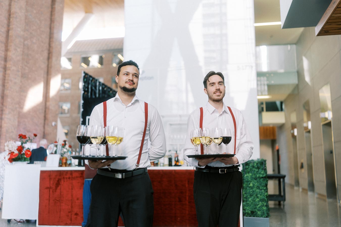 Two servers in white shirts and red suspenders hold trays with glasses of white and red wine at Ricarda’s, Toronto, during the Toronto Prep Forever Launch Party.