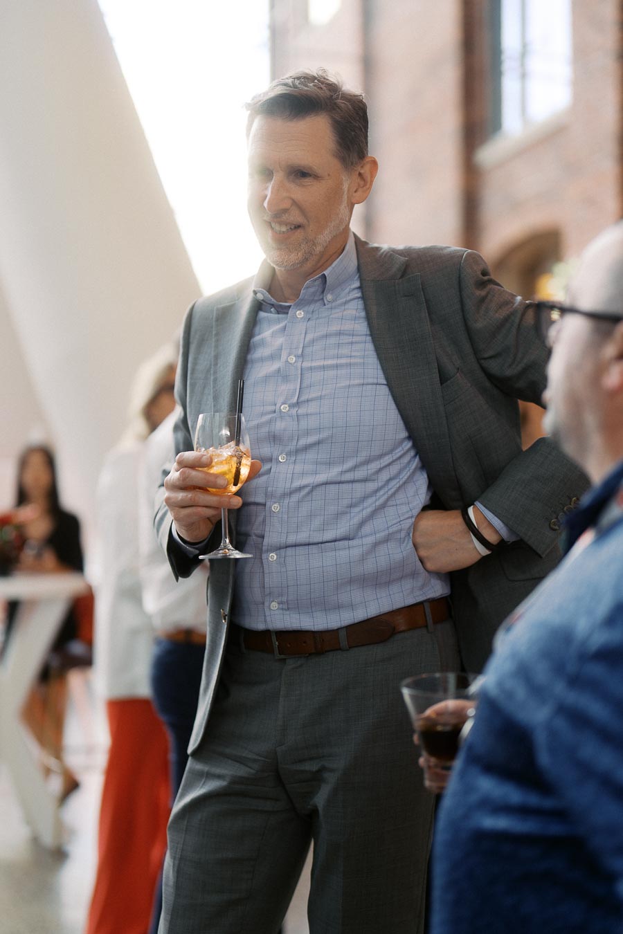 A man in a grey suit holding a drink and speaking with another guest at the Toronto Prep Forever Launch Party at Ricarda’s event space.