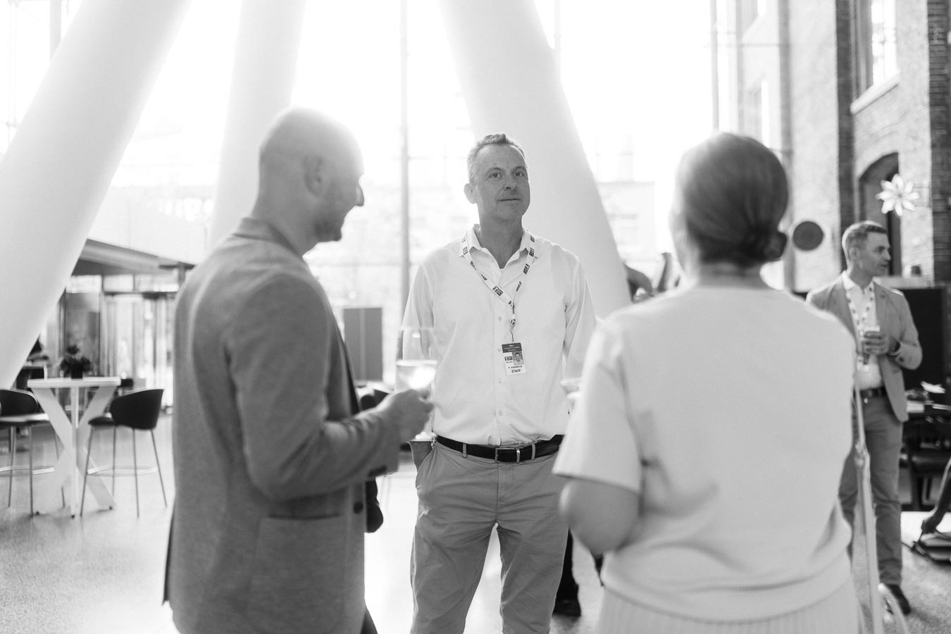 Three adults stand in conversation at Ricarda’s Atrium during the Toronto Prep Forever Launch Party, with modern architecture and natural light in the background.