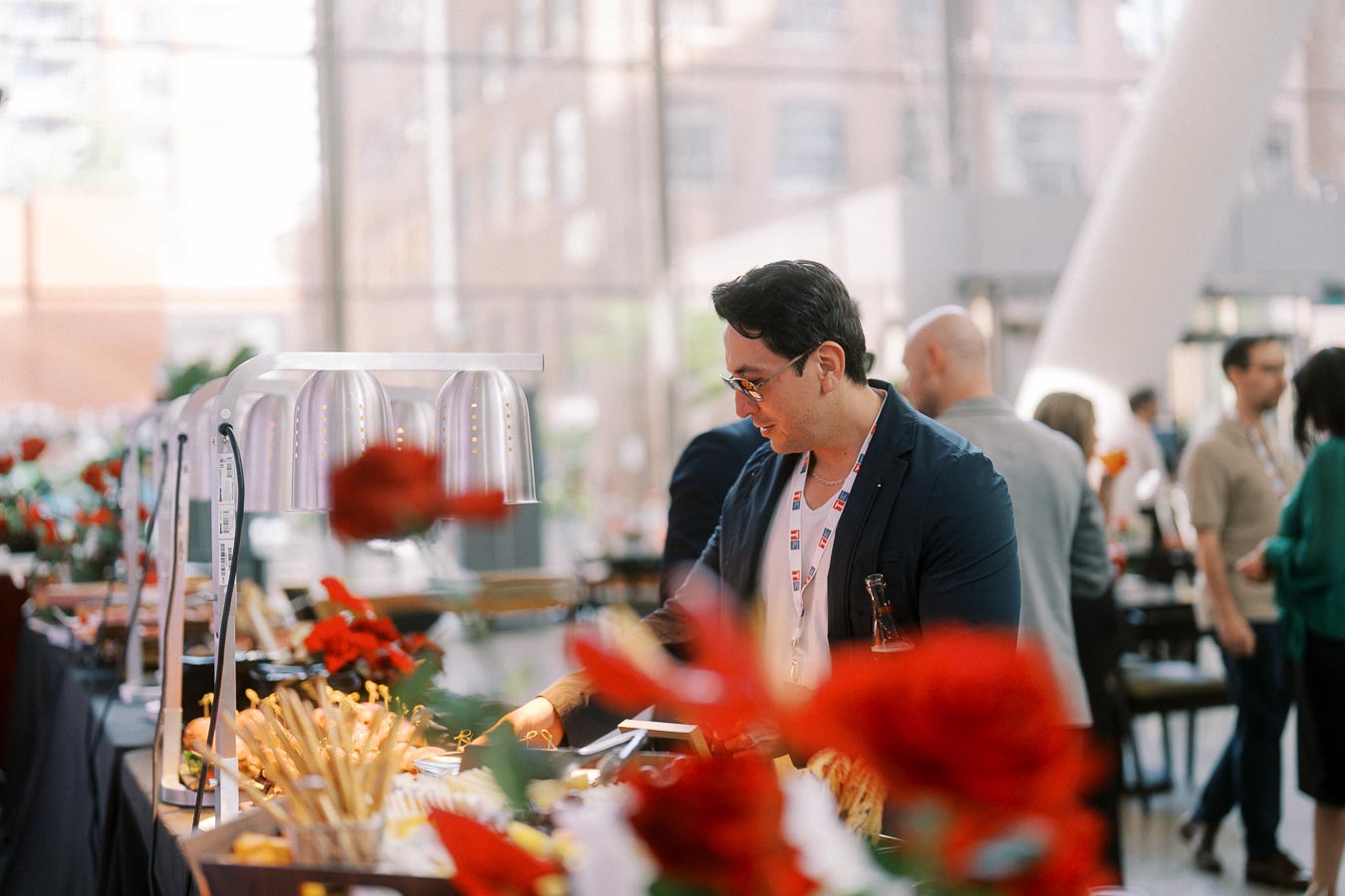 Man with lanyard serves himself at a buffet table decorated with red flowers during a Toronto Prep School event at Ricarda’s Atrium.