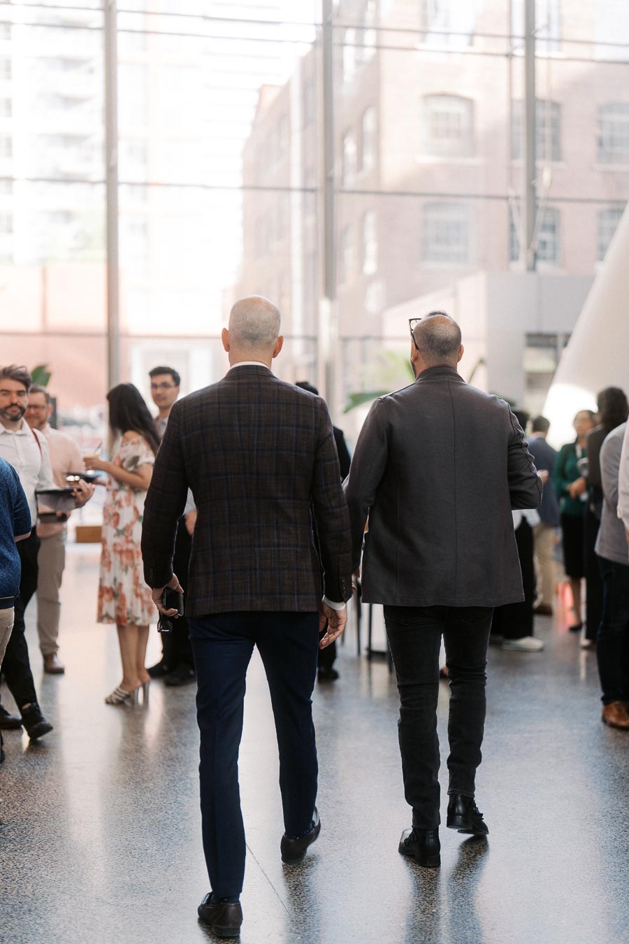 Two men walk through a modern glass atrium at Ricarda’s in Toronto, surrounded by guests networking at the Toronto Prep Forever Launch Party.