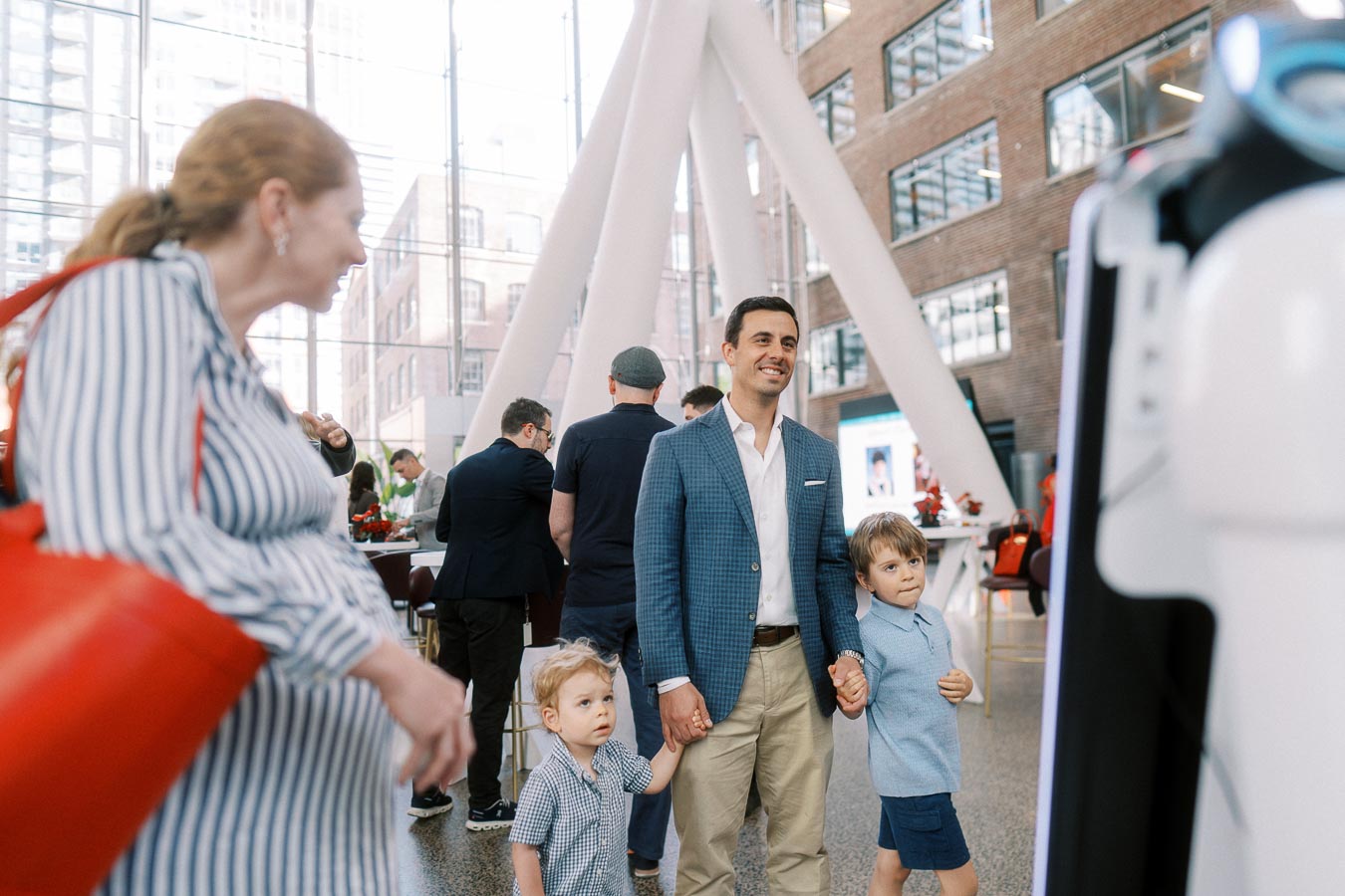 A man in a blue blazer holds hands with two young children inside The Atrium at Ricarda’s during the Toronto Prep Forever Launch Party, surrounded by guests and modern architecture.