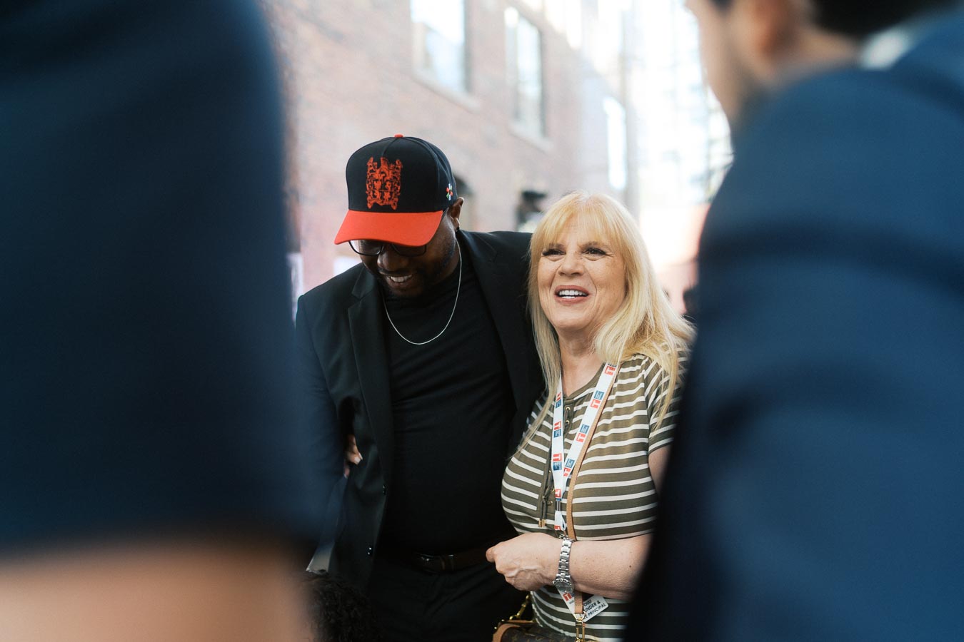 Two guests, one in a striped shirt and another in a black jacket with a Toronto Prep School cap, smiling and conversing at Ricarda’s event in Toronto.