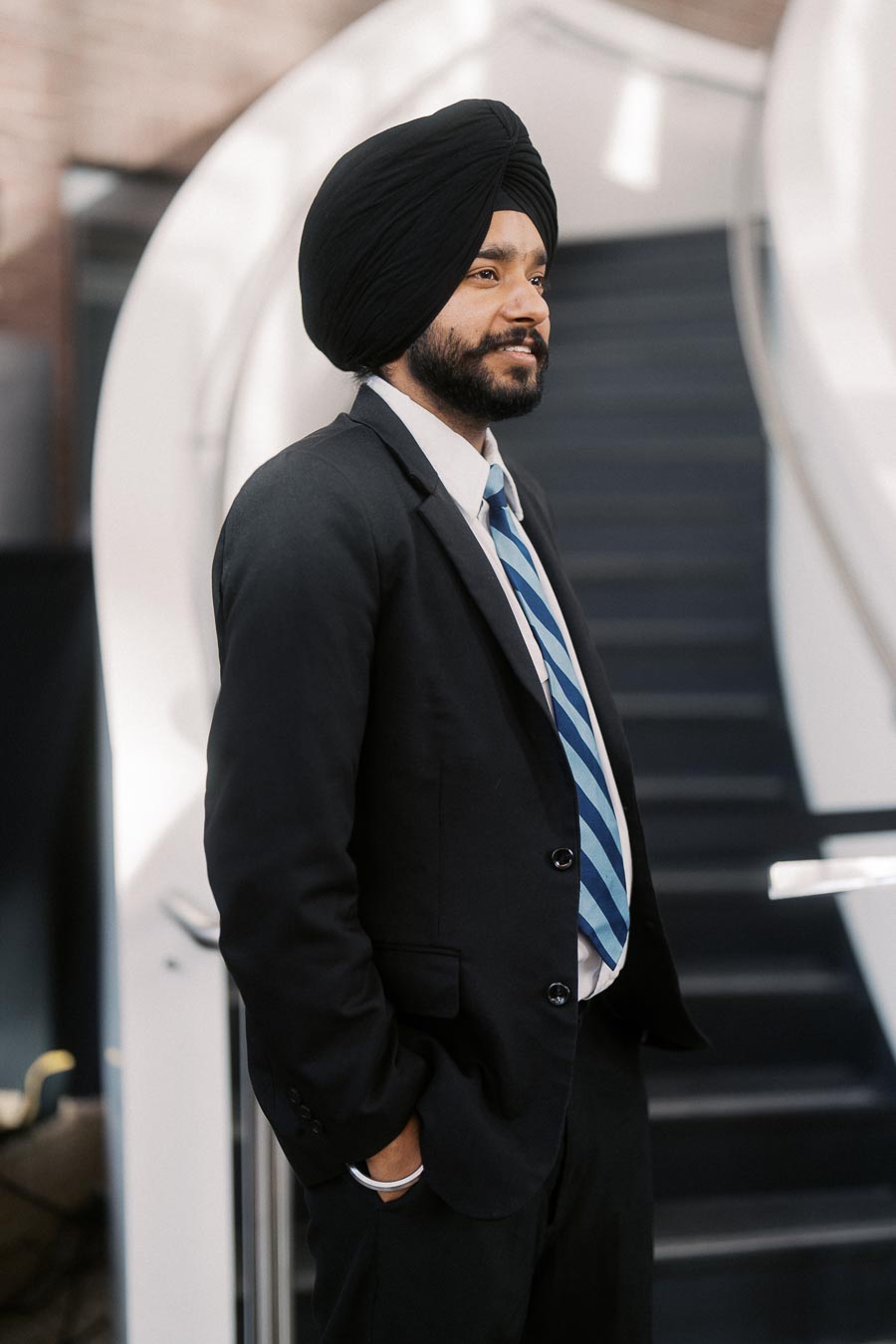 A man in a suit and striped tie stands with hands in pockets by a modern staircase at Ricarda’s during the Toronto Prep School launch event.