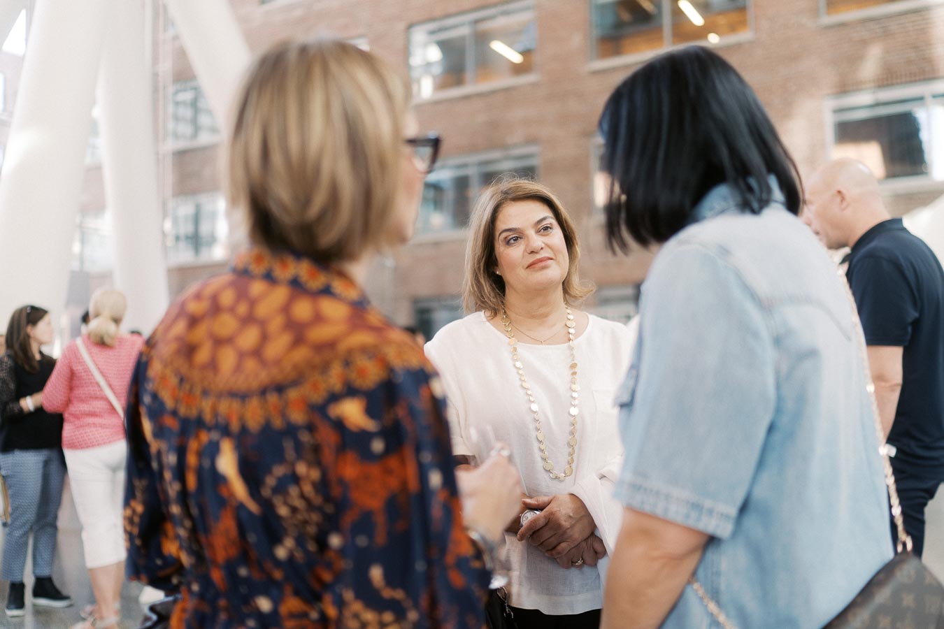 Three women converse in a modern atrium space at Ricarda’s during the Toronto Prep School launch event, with other attendees visible in the background.