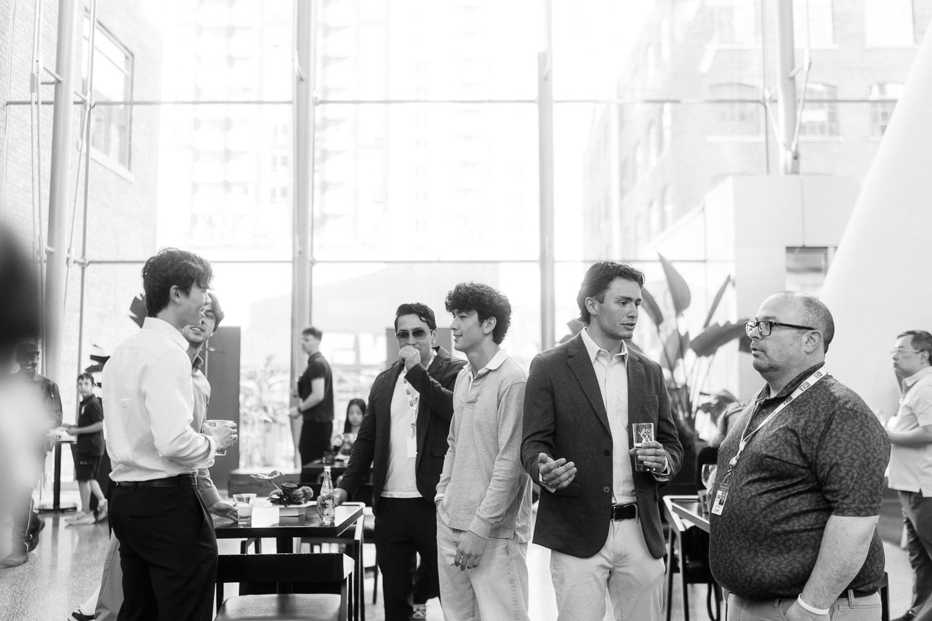 A group of adults and young men converse and network in the sunlit atrium of Ricarda’s in Toronto during the Toronto Prep Forever Launch Party.
