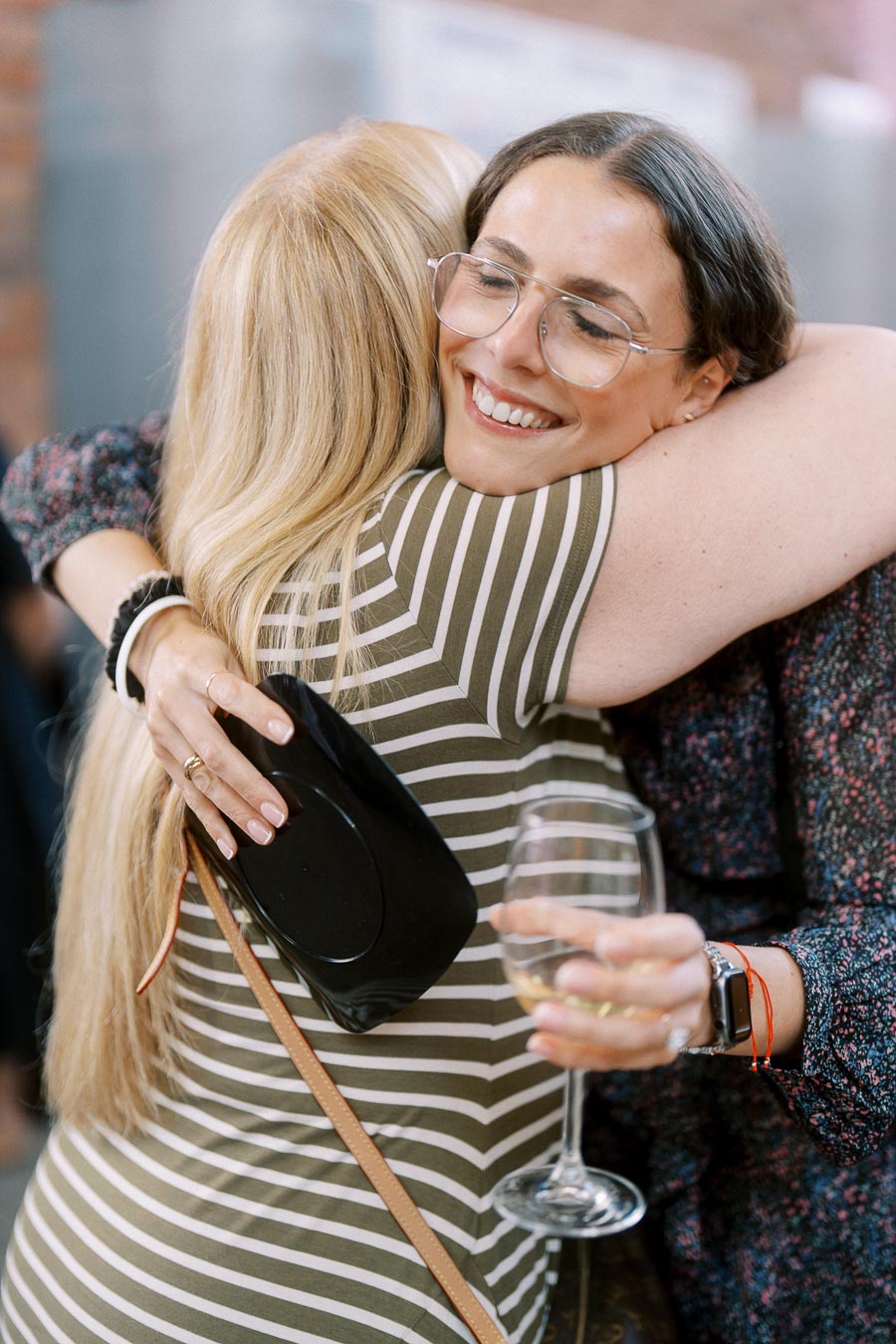 Two women hugging closely, one smiling with eyes closed and holding a wine glass, at the Toronto Prep Forever Launch Party at Ricarda’s in Toronto.