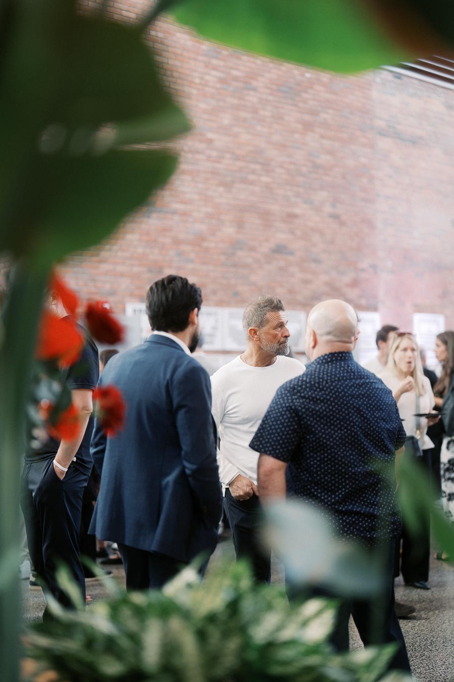 A group of guests engage in conversation at the Toronto Prep Forever Launch Party at Ricarda’s, with greenery and brick walls in the background.