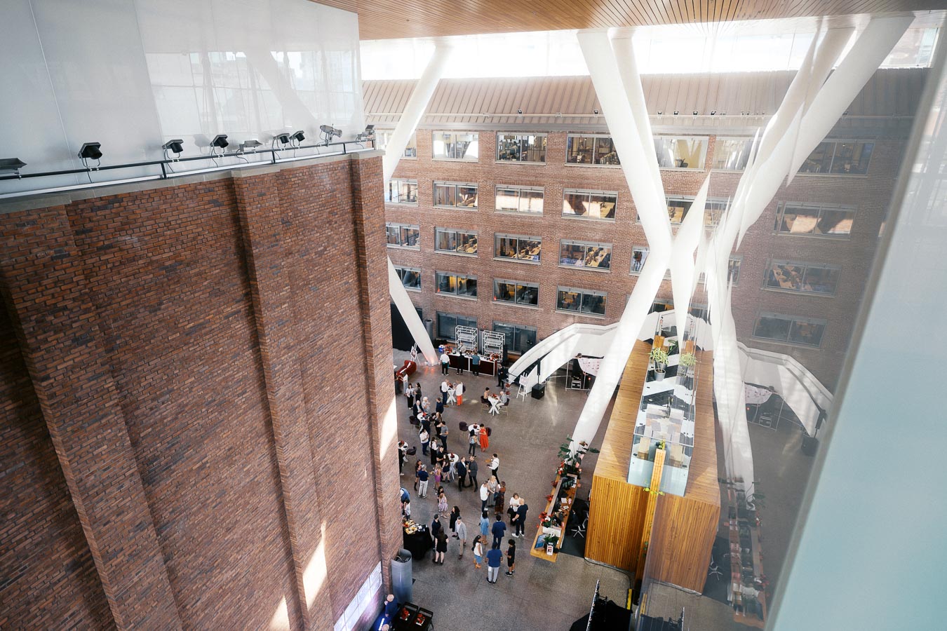 Overhead view of guests gathering in the modern atrium of Ricarda’s, Toronto, with brick walls, glass ceiling, and architectural columns during the Toronto Prep School event.