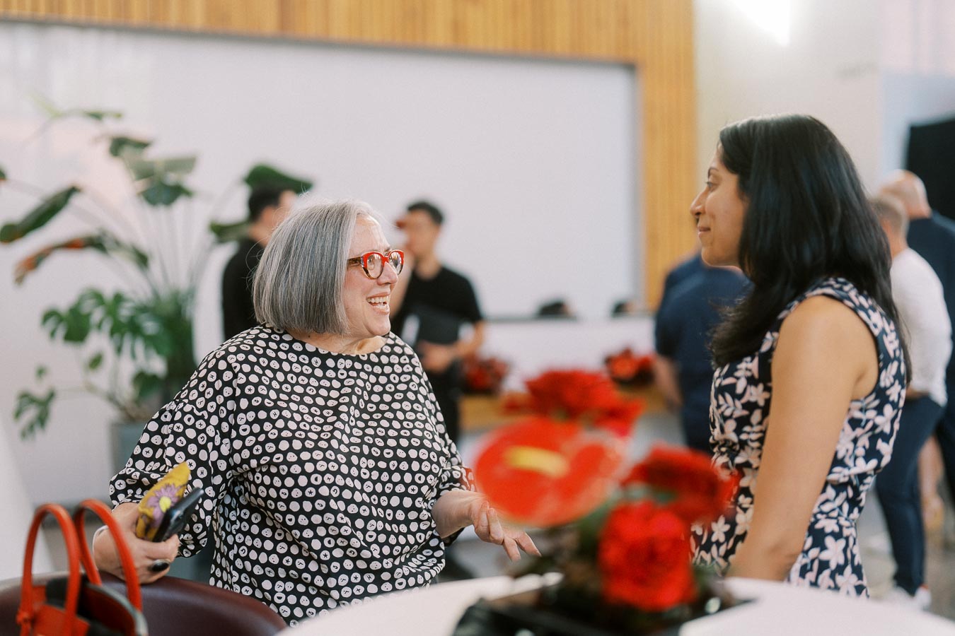 Two women engaged in conversation at a Toronto Prep School event, with floral centrepieces and guests mingling in the background at Ricarda’s.