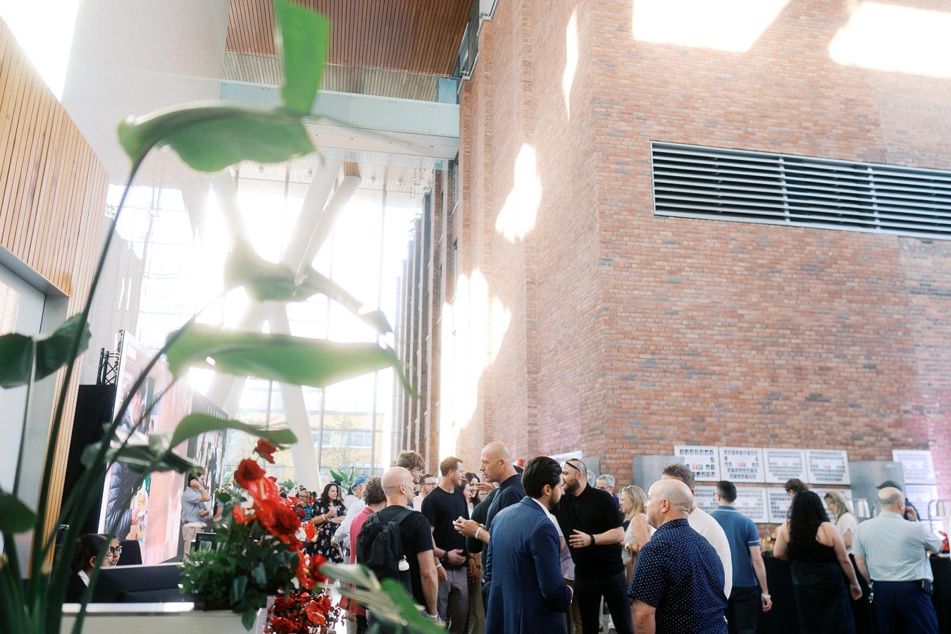 Guests networking in the modern atrium at Ricarda’s Toronto, with brick walls, large windows, and floral decor during the Toronto Prep Forever Launch Party.