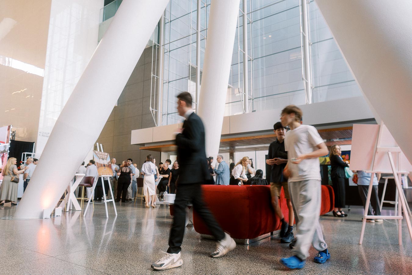 Guests and students mingle in the bright, modern atrium at Ricarda’s in Toronto during the Toronto Prep Forever Launch Party, with architectural columns and red lounge seating visible.