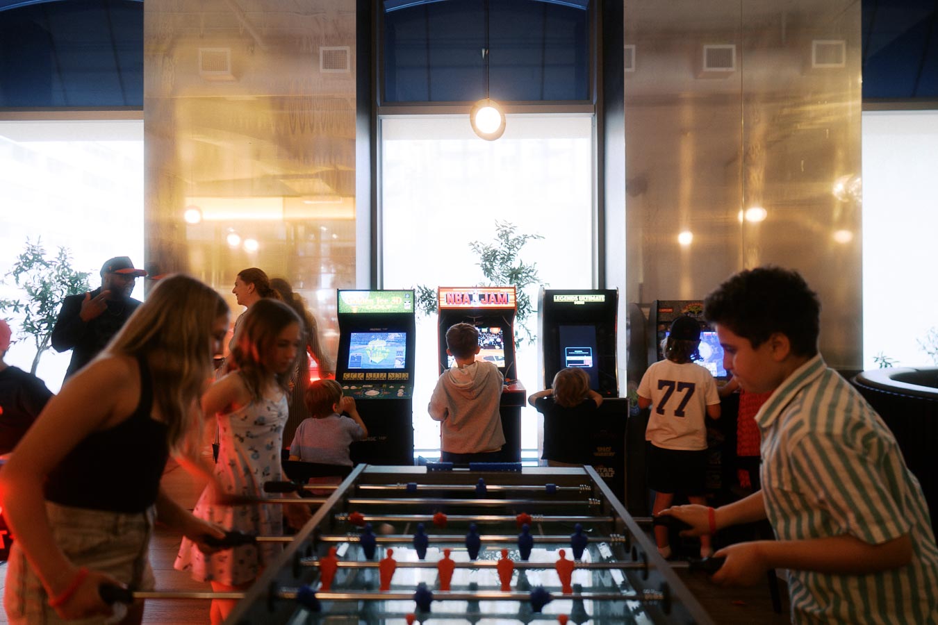 Children gathered around foosball and arcade games in a modern event space at Ricarda’s, Toronto, during the Toronto Prep Forever Launch Party.