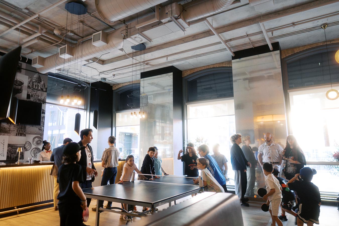 Children playing ping pong and adults socializing in a modern lounge at Ricarda’s, Toronto, during the Toronto Prep Forever Launch Party.