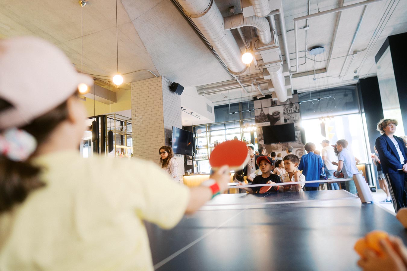 Children playing ping pong at Ricarda’s in Toronto during the Toronto Prep Forever Launch Party, with families and guests in the background.