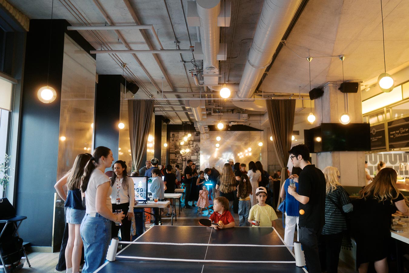 Children and adults gather around a ping pong table and activity stations at Ricarda’s in Toronto during the Toronto Prep Forever Launch Party, with a lively event atmosphere.