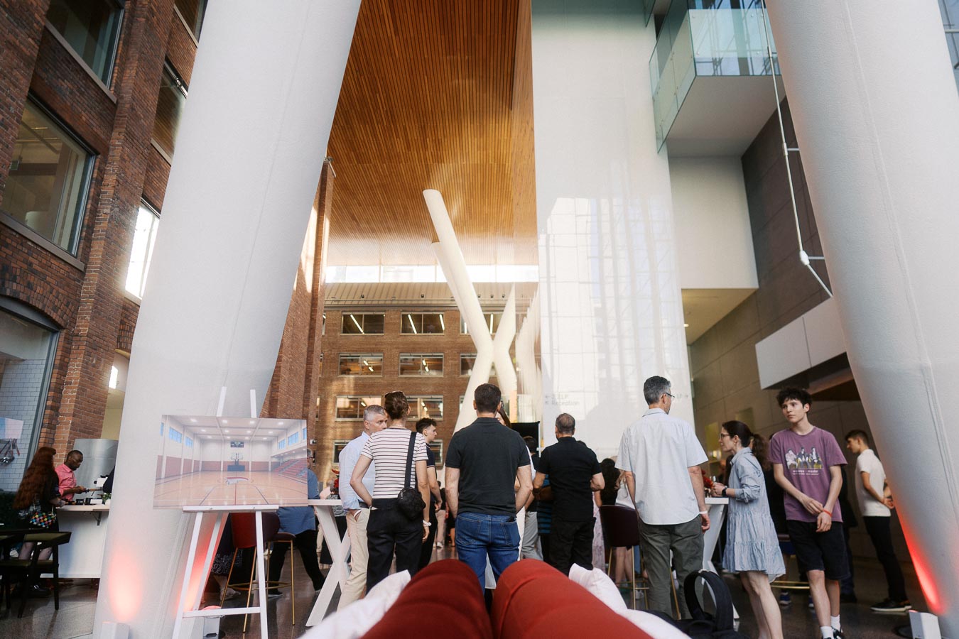 A group of people socialize in the modern atrium of Ricarda’s Restaurant in Toronto, surrounded by tall white columns, brick walls, and a wood ceiling during a school event.