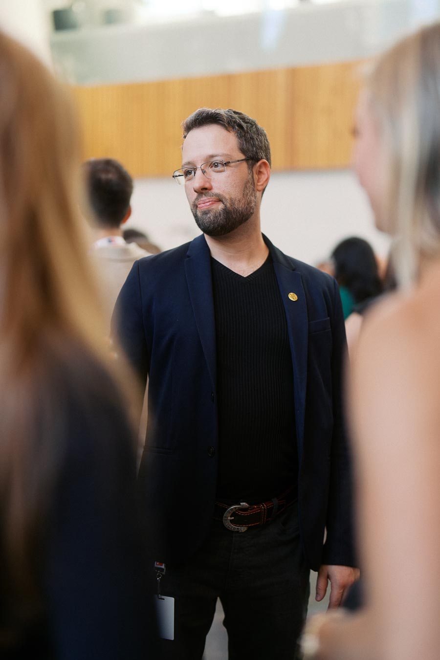A man in a navy blazer and glasses stands in conversation at the Toronto Prep Forever Launch Party at Ricarda’s in Toronto, with other guests blurred in the foreground.