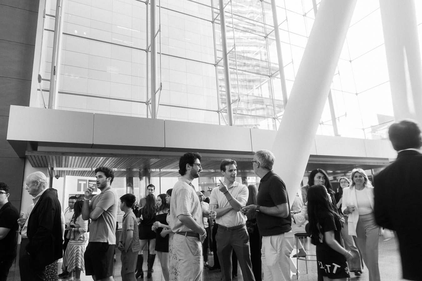 A diverse group of guests, including adults and children, gather and converse in the bright glass atrium of Ricarda’s during the Toronto Prep Forever Launch Party in Toronto.