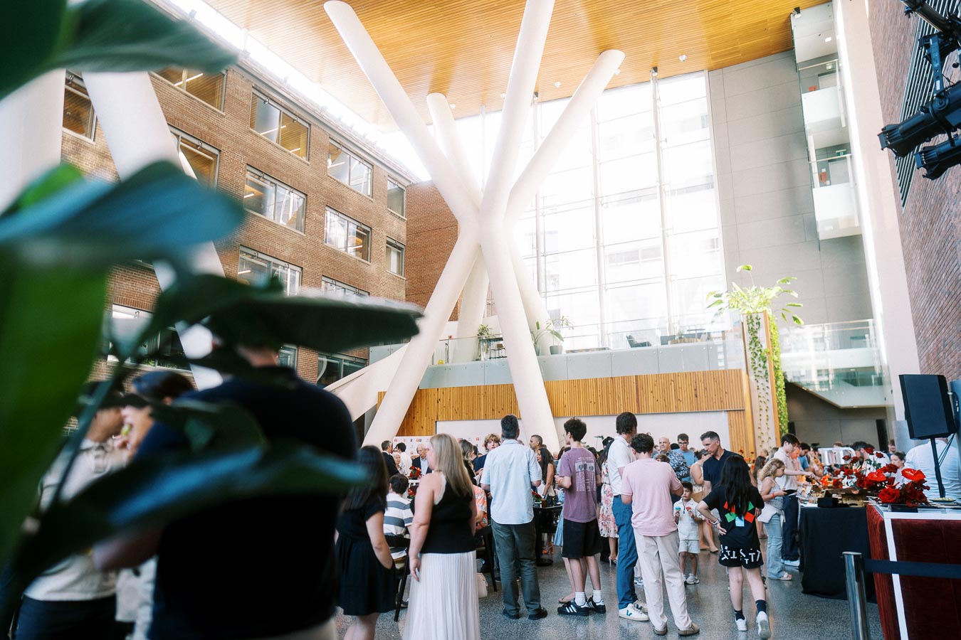 A lively crowd mingles in the modern atrium of Ricarda’s Restaurant, Toronto, during the Toronto Prep Forever Launch Party. Large white pillars, brick walls, and greenery are visible.