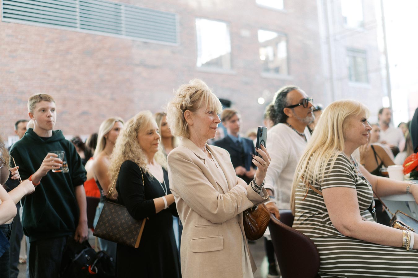 A diverse group of Toronto Prep School community members attentively watch a presentation at Ricarda’s, with one woman photographing the event.