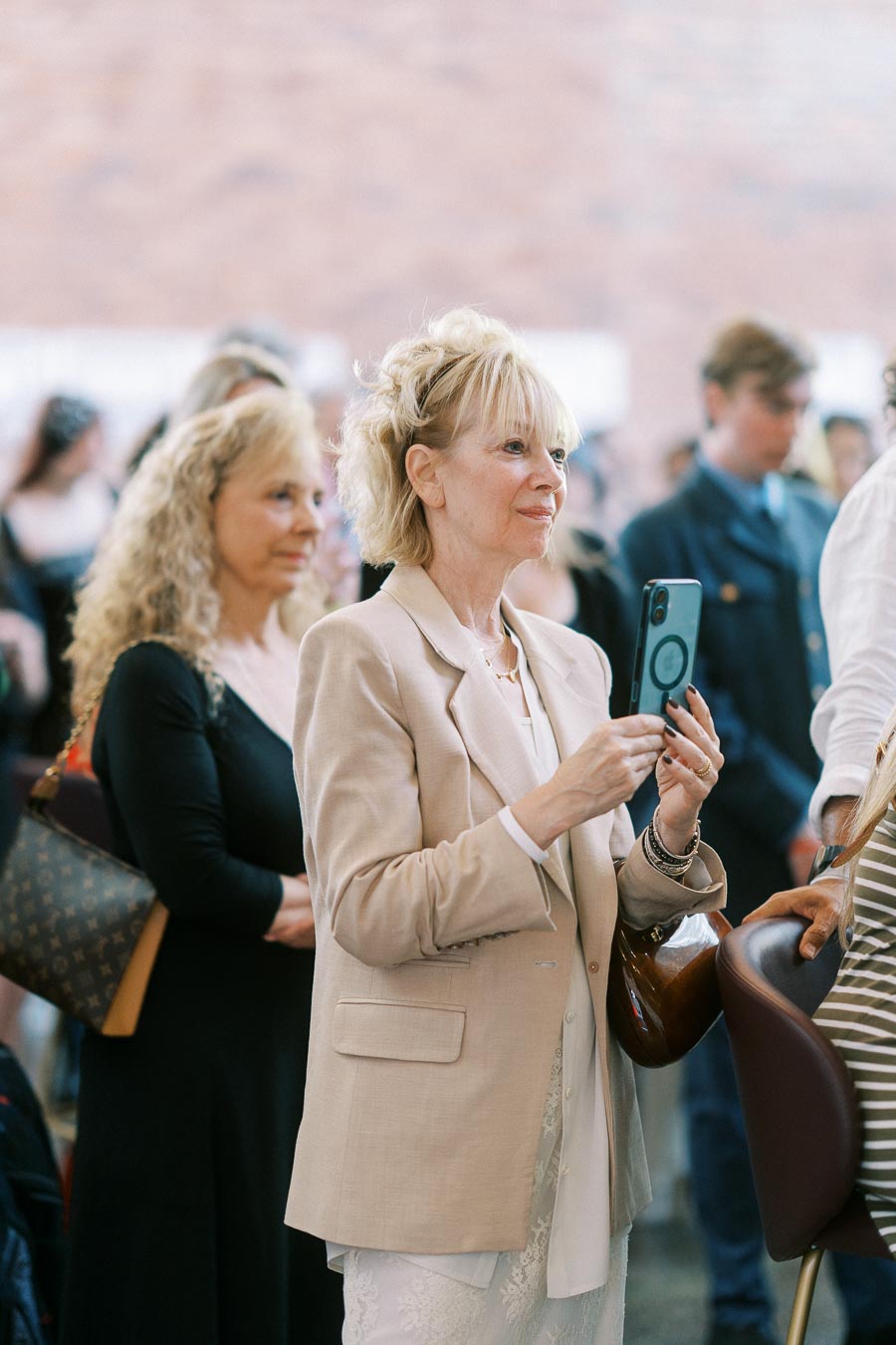 A woman in a beige blazer takes a photo with her phone among a group of guests at the Toronto Prep Forever Launch Party at Ricarda’s in Toronto.