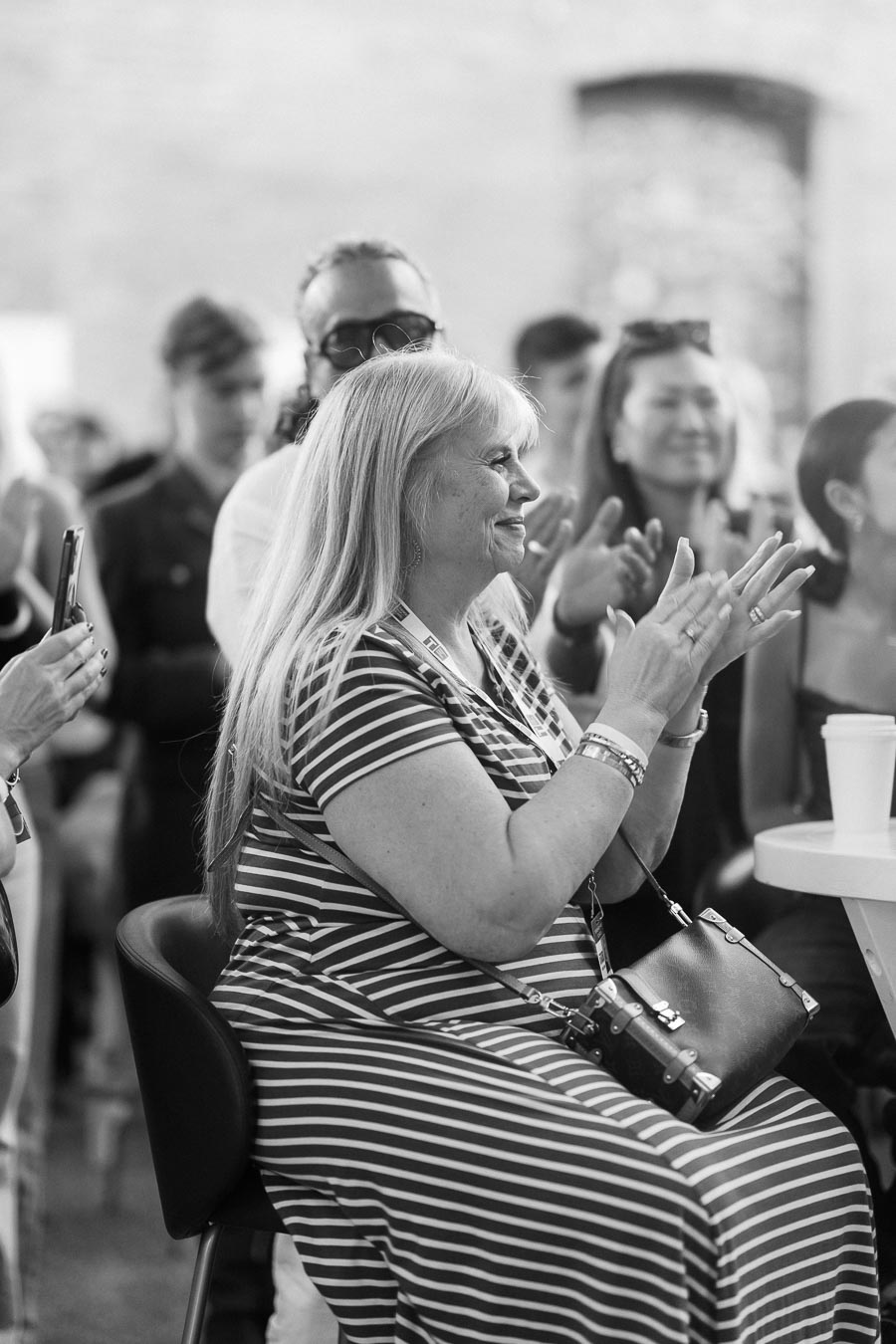 A woman in a striped dress claps while seated at a table, surrounded by other applauding attendees at the Toronto Prep Forever Launch Party at Ricarda’s in Toronto.