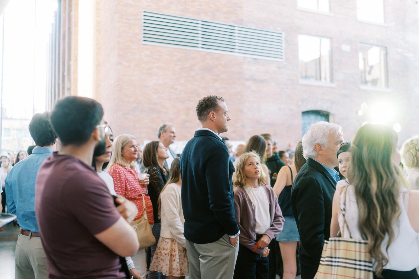 A diverse group of adults and children stand together in the modern atrium at Ricarda’s, Toronto, attending the Toronto Prep Forever Launch Party.