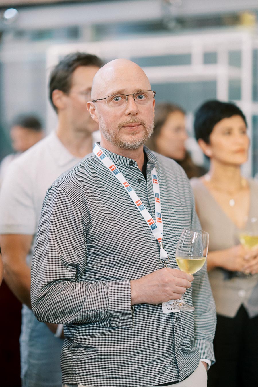 A Toronto Prep School staff member wearing a lanyard and glasses holds a glass of white wine at the Forever Launch Party at Ricarda’s in Toronto.