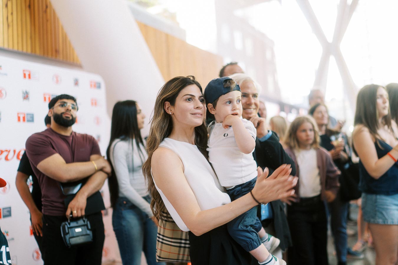 A woman holding a young child in a crowd, both watching and clapping during the Toronto Prep Forever Launch Party at Ricarda’s in Toronto.