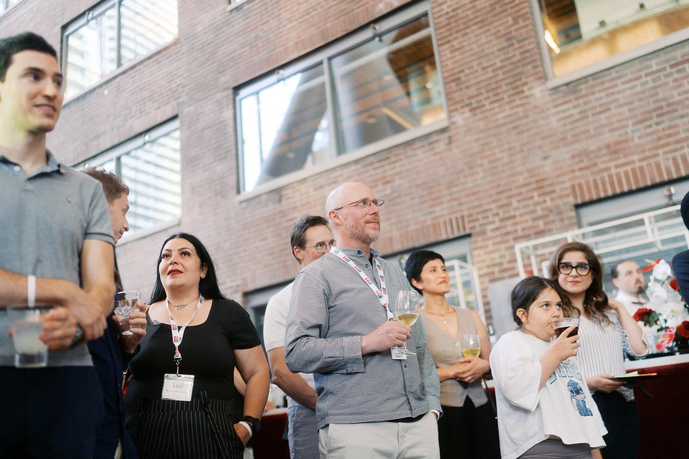A group of adults and a child stand together, watching an event presentation at The Atrium at Ricarda’s in Toronto during the Toronto Prep Forever Launch Party.