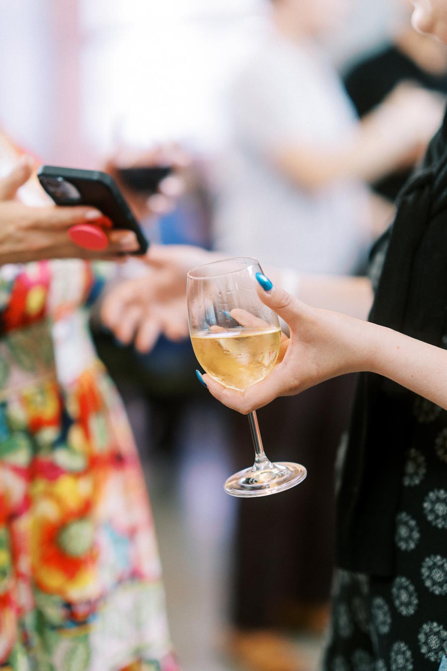 Close-up of two guests at Ricarda’s in Toronto, one holding a glass of white wine, the other holding a smartphone, during the Toronto Prep Forever Launch Party.